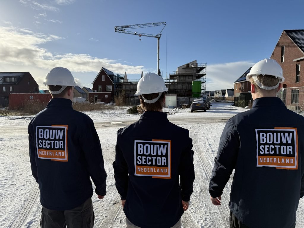 Drie mannen van Bouwsector Nederland van achteren gezien bij een bouwkraan en woningen in aanbouw
