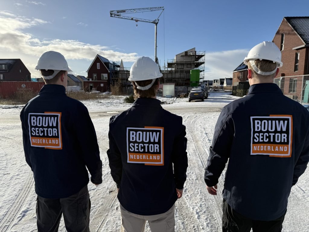 Drie vakmensen van Bouwsector Nederland in donkere jassen en witte helmen voor nieuwe woningen in de sneeuw